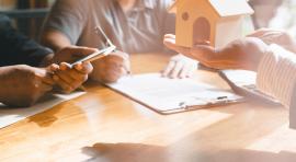 Trois personnes autour d'une table dont une qui tient une petite maison pour illustrer le compromis de vente