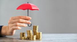 Photo d'une main qui tient un mini parapluie au-dessus de tas de pièces de monnaie