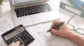 Photo de mains tenant un stylo et devant un ordinateur et une calculatrice pour investir en assurance vie