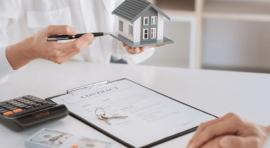 Mains de personnes avec une maquette de maison et une calculatrice devant eux