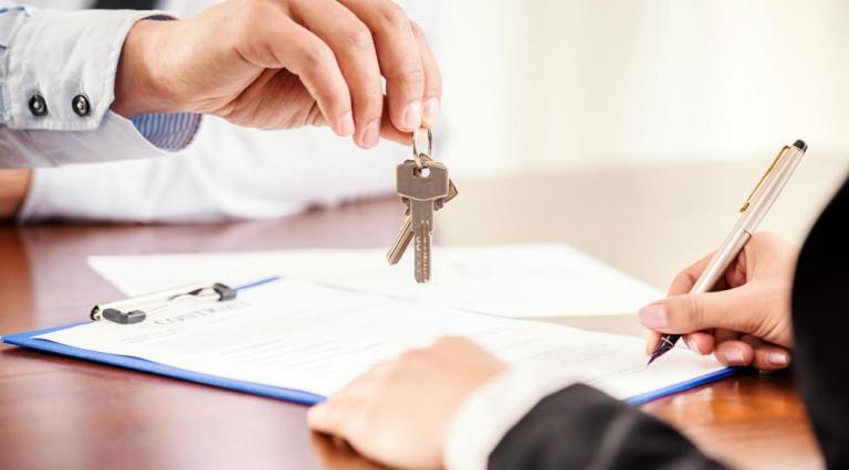 Mains de deux personnes au moment d'une signature d'un contrat avec remise de clés