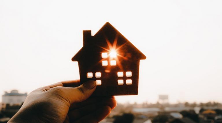 figurine de maison pointé devant une paysage vers le soleil