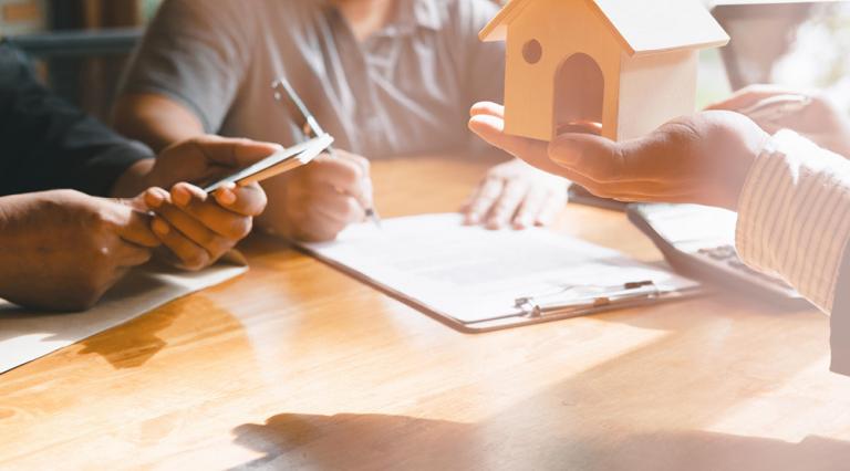 Trois personnes autour d'une table dont une qui tient une petite maison pour illustrer le compromis de vente