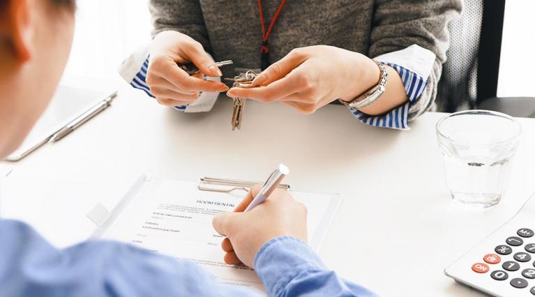 Mains de deux personnes au moment d'une signature d'un contrat avec remise de clés