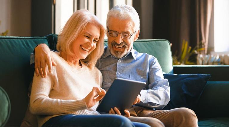 Photo d'un couple de sexagenaires sur canapé avec une tablette