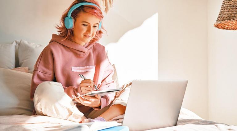 Photo d'une jeune étudiante sur son lit face à son ordinateur