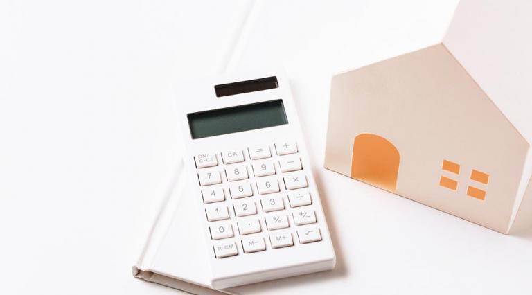 Calculatrice posée sur un livre à côté d'une maquette de maison