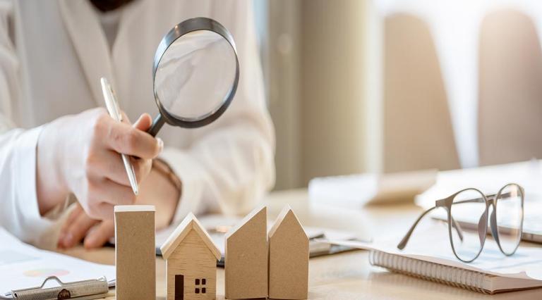 Photo d'une personne tenant une loupe au-dessus de maquettes de maisons