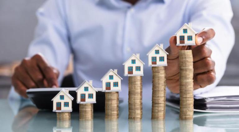 Mains posant des maquettes de maisons sur des tas de pièces de monnaie