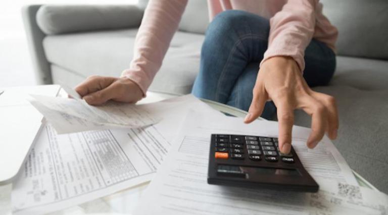 Mains sur une calculatrice et personne devant des feuilles de papier