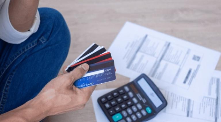 Mains d'une personne tenant des cartes bancaires devant des feuilles et une calculatrice