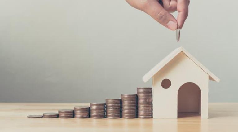 Main qui empile des pièces à côté d'une maquette de maison eligible Pinel Plus