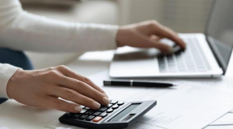 Photo d'une personne devant un ordinateur et une calculette