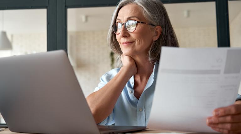 Femme devant un ordinateur tenant des documents de PER et devant un ordinateur