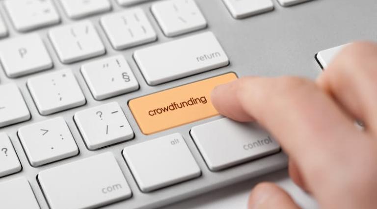 Mains en train d'appuyer sur une touche crowdfunding sur un clavier d'ordinateur