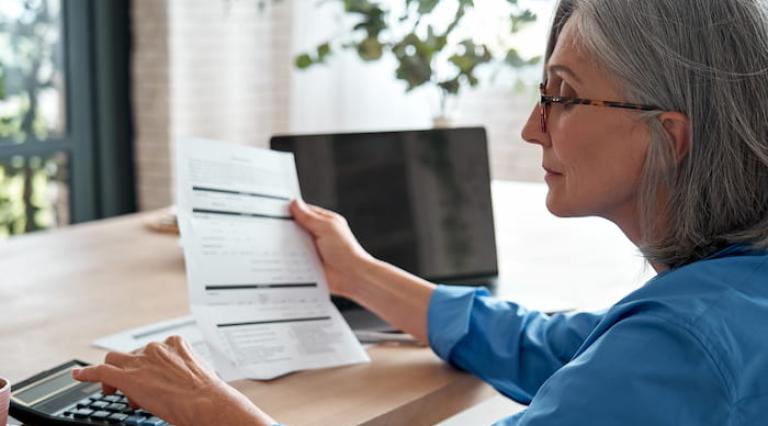 Femme lisant un contrat d'assurance ou de PER et utilisant une calculatrice 