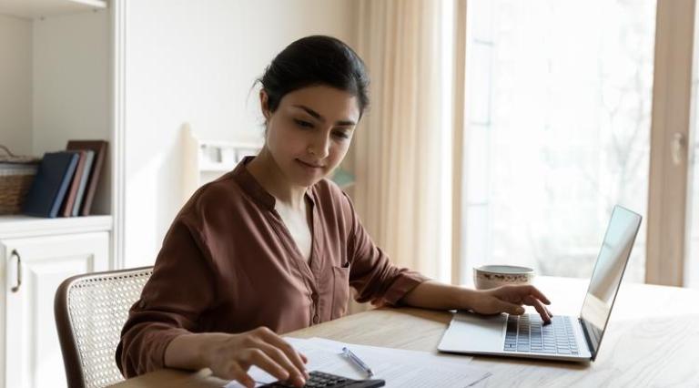 Photo d'une femme en train de taper sur une calculatrice et un ordinateur pour souscrire un compte a terme