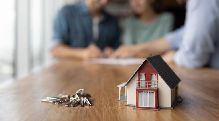 Photo d'un trousseau de clés posé sur une table à côté d'une maquette de maison illustrant un achat immobilier