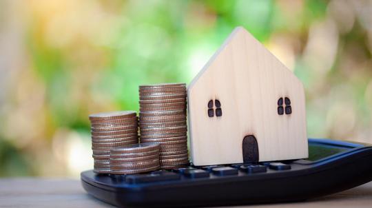 Photo d'une maquette de maison posée à côté de tas de pièces de monnaie