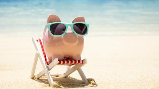 Cochon tirelire posé sur un transat avec des lunettes de soleil sur une plage