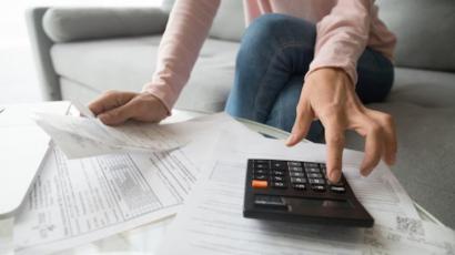 Mains sur une calculatrice et personne devant des feuilles de papier