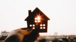 main tenant une figurine représentant une maison vers le ciel