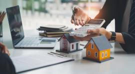 Personne tenant une calculatrice devant un ordinateur et des maisons illustrant l achat immobilier