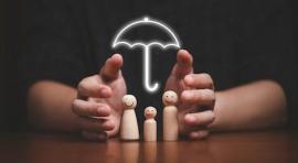 Mains qui entourent des silhouettes en bois d'un couple avec un enfant, avec un parapluie au-dessus d'eux illustrant l'assurance vie