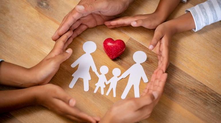 Des mains qui se tiennent autour d'une famille en papier au cœur