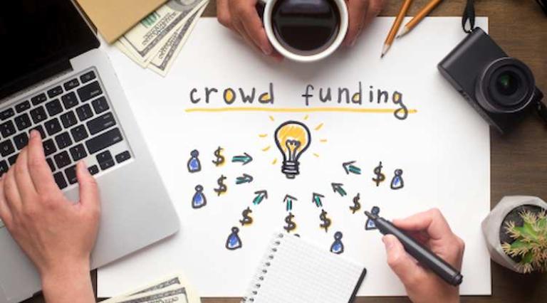 Photo d'un ordinateur posé à côté d'une inscription sur le crowdfunding