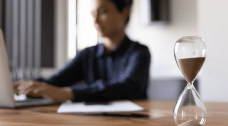 Femme devant son ordinateur avec un sablier au premier plan