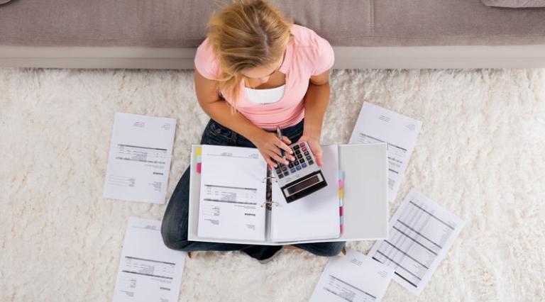 Femme assise en tailleur avec des papiers et une calculatrice analysant ses livrets d'epargne