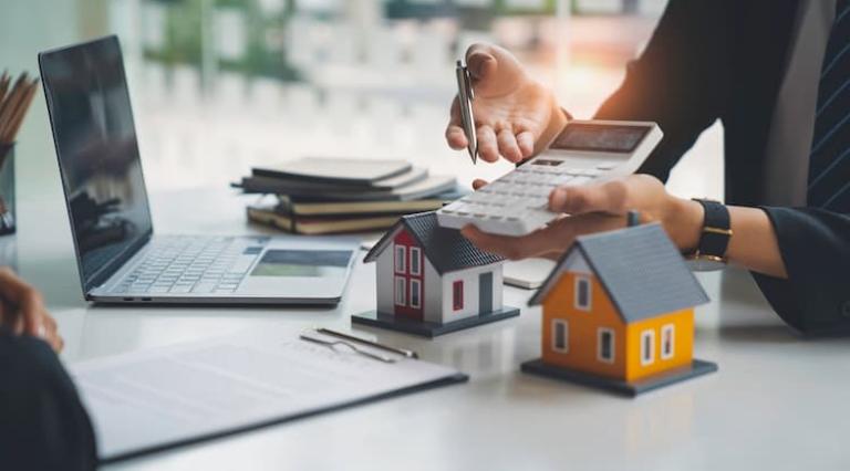 Personne tenant une calculatrice devant un ordinateur et des maisons illustrant l achat immobilier