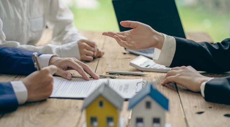 Photo de mains au dessus d'un contrat d investissement locatif et à côté de maquettes de maisons