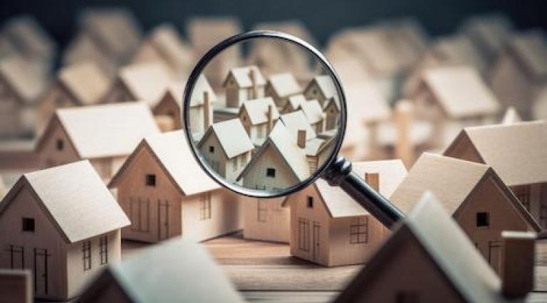 Photo d'une loupe qui zoome sur des maquettes de maisons illustrant differents types de biens immobilier