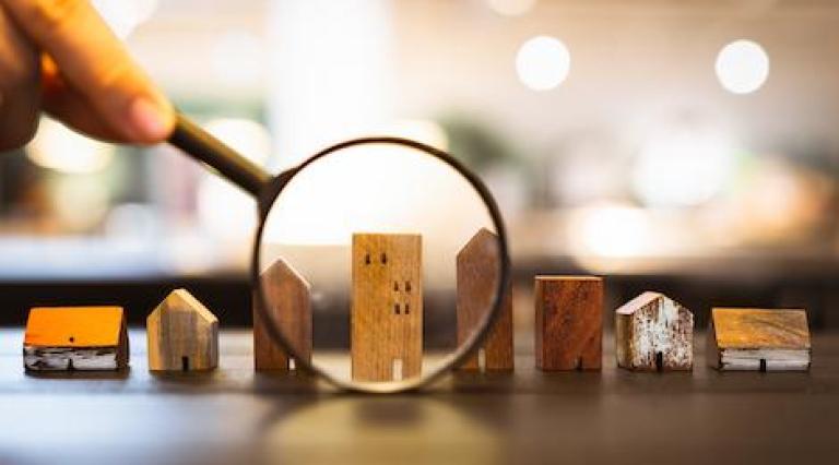 Photo d'une loupe qui zoome sur des maquettes de maisons illustrant l investissement en lmp