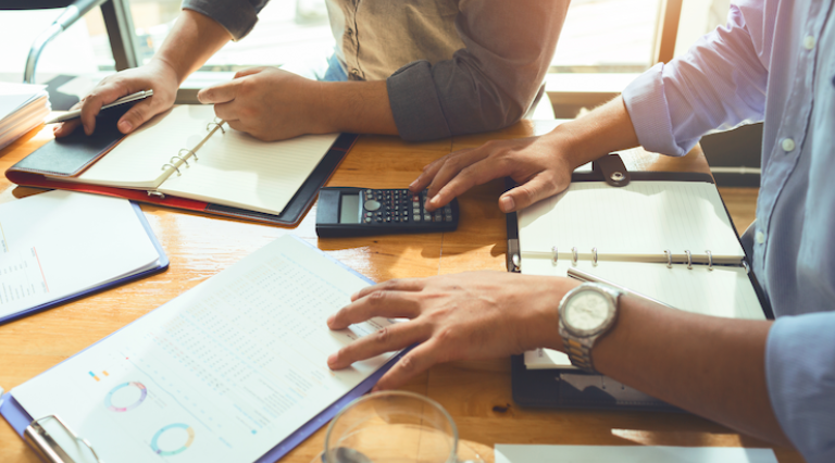 Photo de personnes sur une table de réunion avec calculatrice et graphiques pour des demarches activites LMNP
