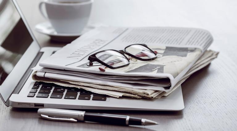 Ordinateur pose sur bureau avec un journal et des lunettes de vue dessus illustrant les actualites d epargne