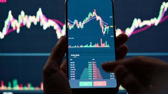 Photo d'un homme avec Smartphone affichant un graphique de bourse à l'écran illustrant un OPCVM